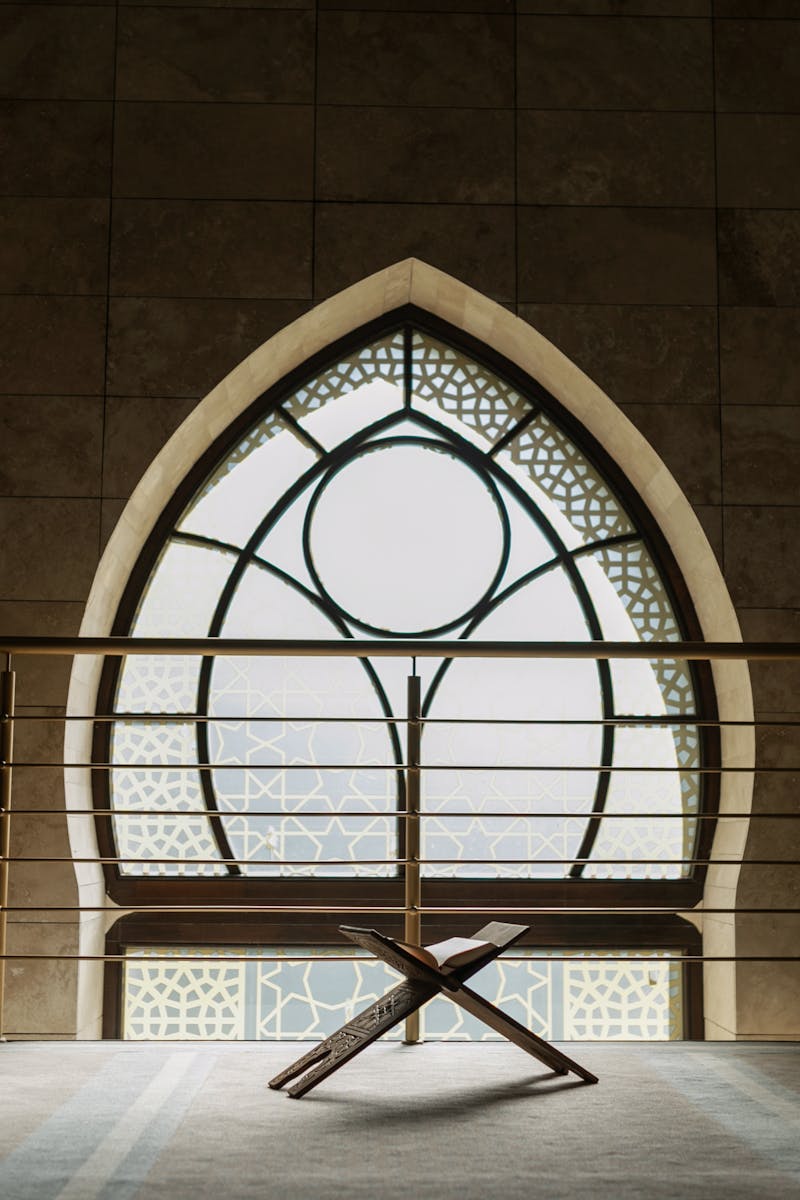 A peaceful mosque interior featuring a backlit window, rehal stand, and intricate architecture.